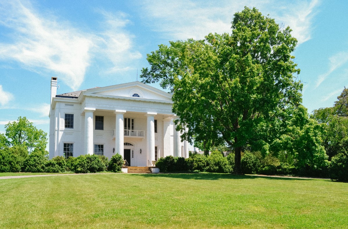 White mansion with pillars overlooking green lawn