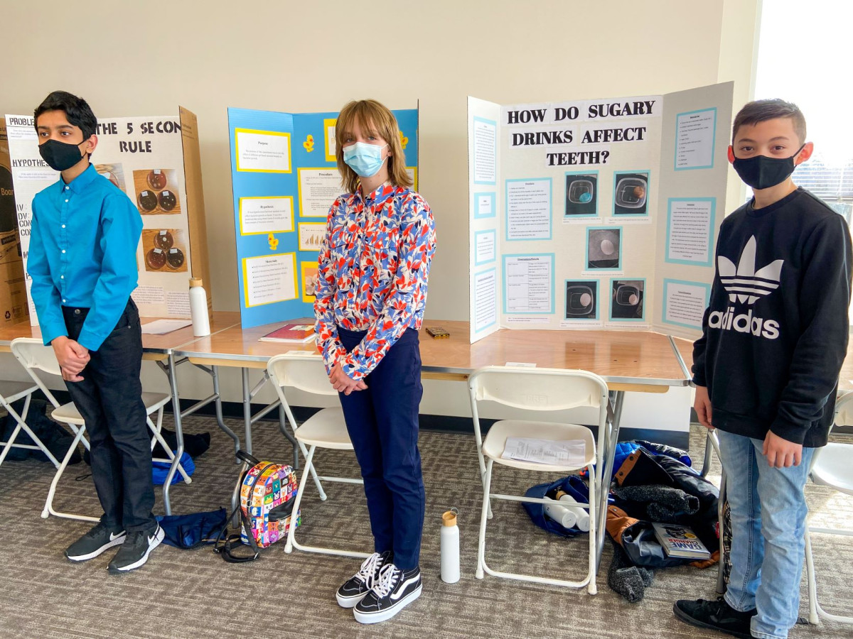 three young students stand in front of science fair projects
