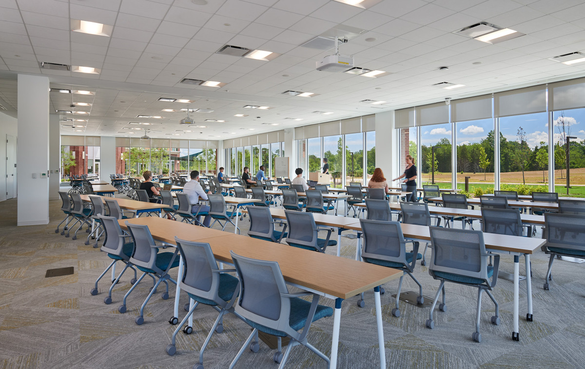 tables and chairs are arranged classroom style in a large conference room surrounded by windows overlooking the trees 