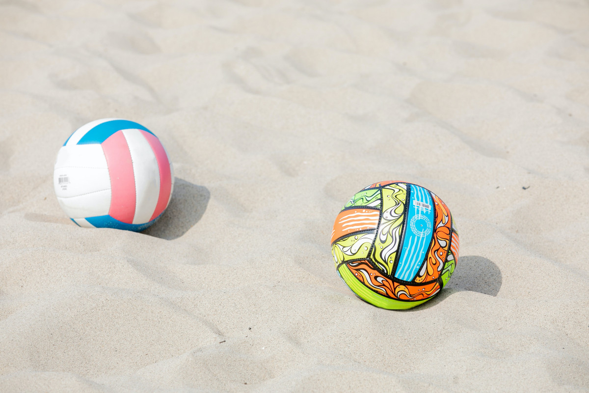 two brightly colored volleyballs atop beach sand