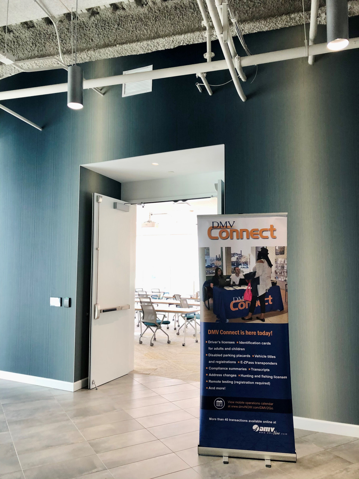 DMV cConnect signs stands outside a conference room with an open door in a welcoming manner