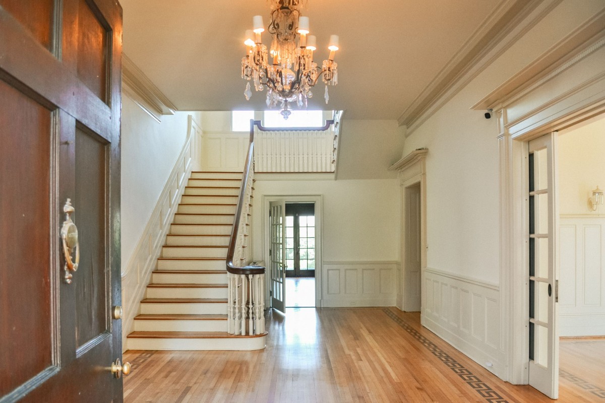 expansive foyer with cream walls, grand staircase, and crystal chandelier