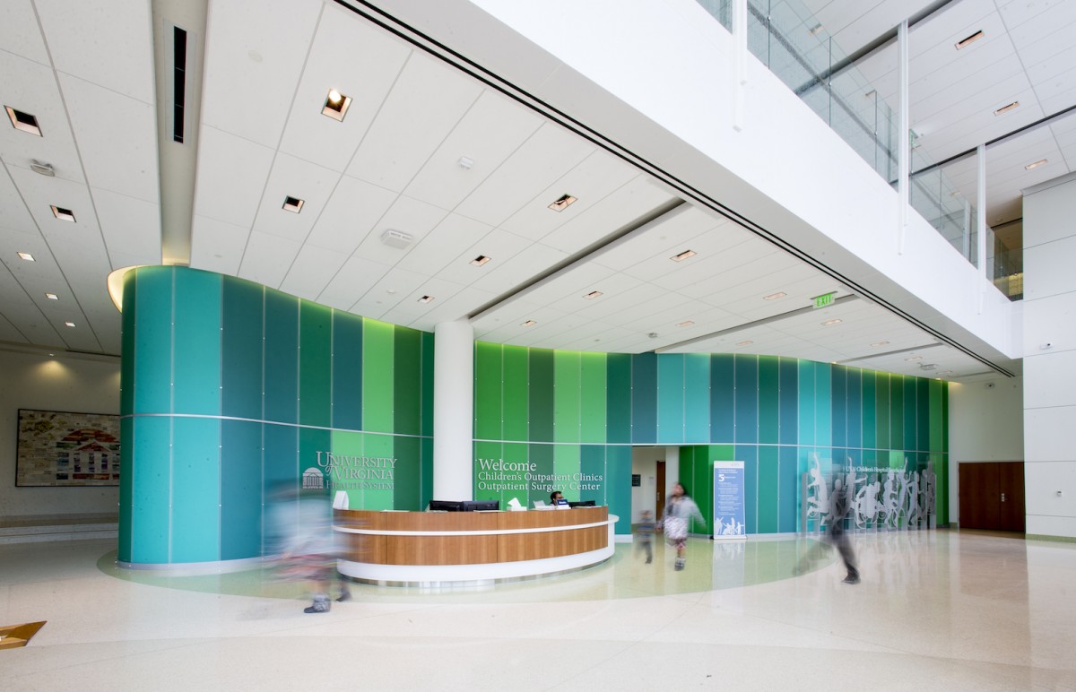 Lobby of a brightly lit, modern space with a maple desk and green wall panels 