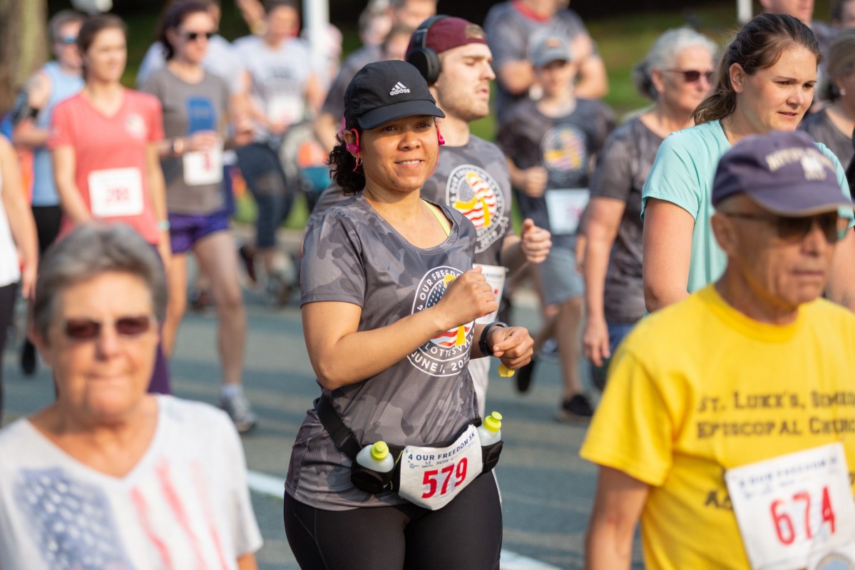 Smiling people run and walk wearing race bibs and athletic gear