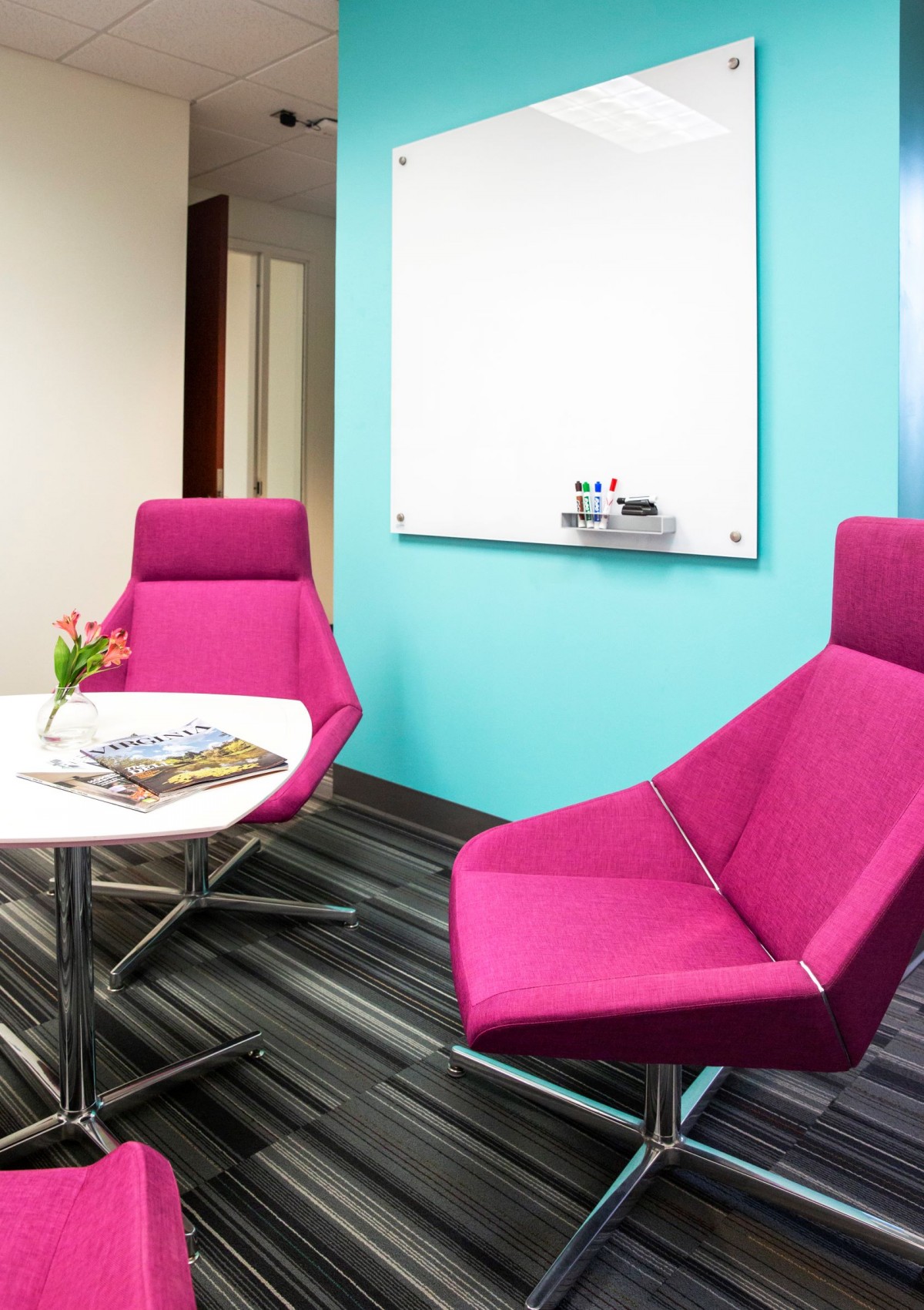 a samll room with futuristic bright pink club chairs and a glass white board on an aqua wall 