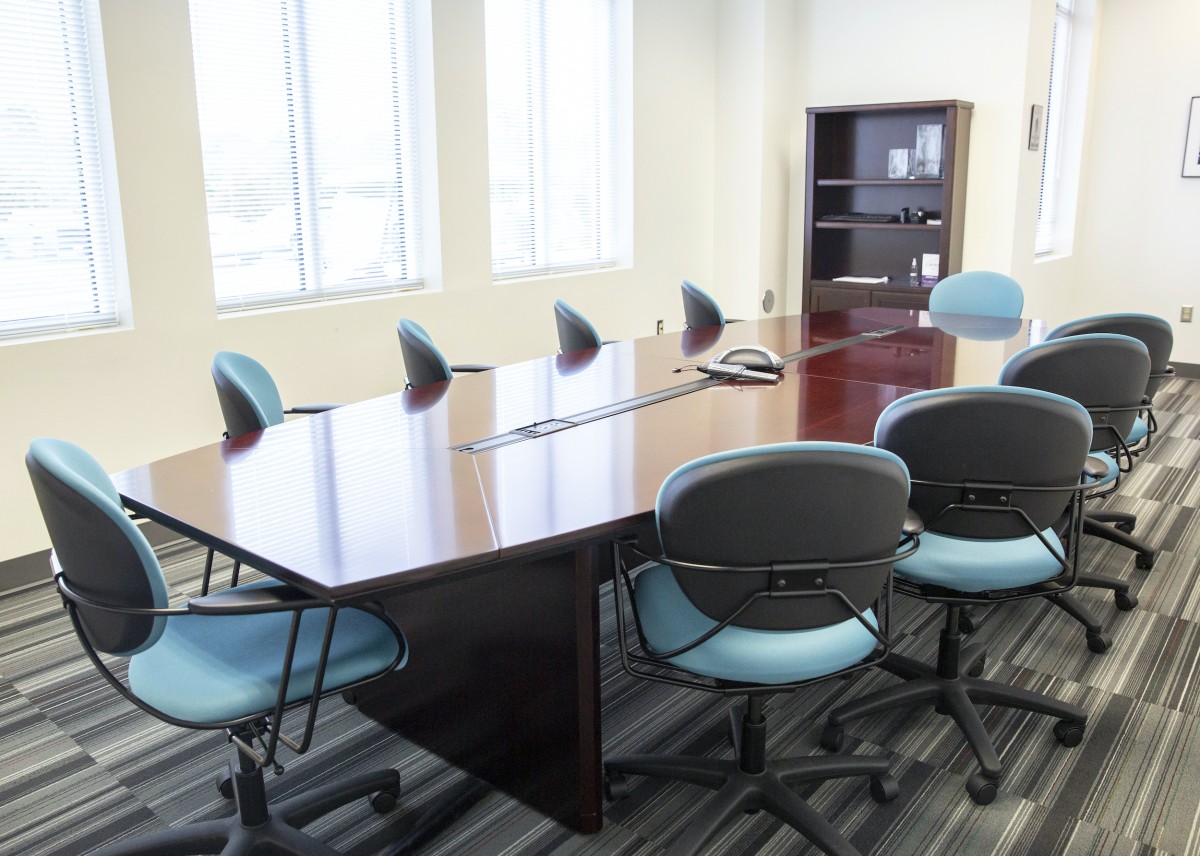 aqua colored chairs surround a polished wood conference table in a sunny white room