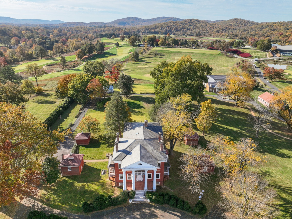 Aerial view of a 19th century brick estate surrounded by rolling green hills and mountains in the background